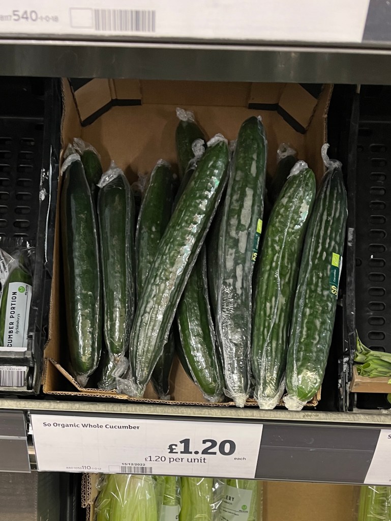 A supermarket shelf containing a box with a few organic cucumbers
